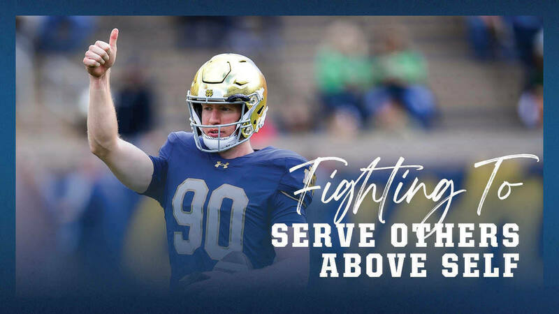 A Notre Dame football player, wearing a gold helmet and a blue jersey with the number 90, gives a thumbs-up on the field. Text overlay reads, "Fighting To Serve Others Above Self."