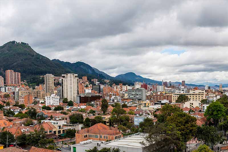 An elevated view of a city with buildings and mountains under a cloudy sky