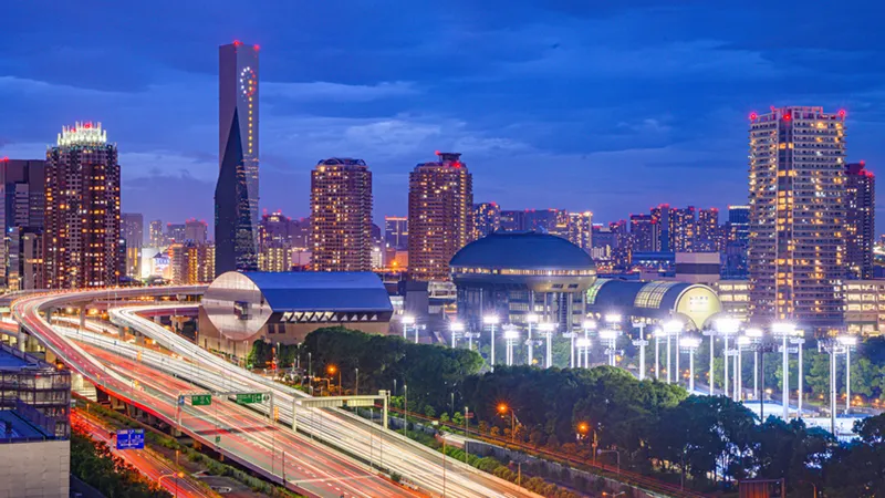 A vibrant Tokyo cityscape at dusk featuring the Fuji Television building and glowing light trails from traffic on a multi-lane highway.