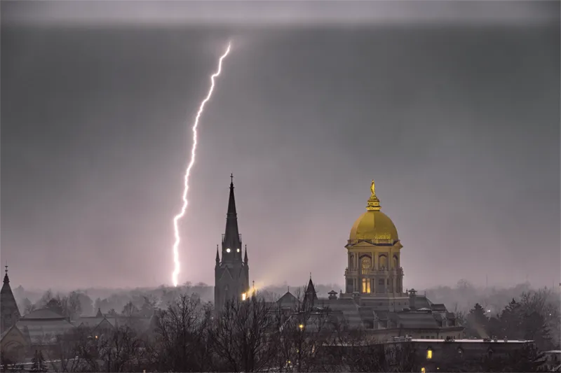 A single bolt of lighting strikes behind the main building and the Basilica of the Sacred Heart on a foggy and stormy evening near the campus of the University of Notre Dame.