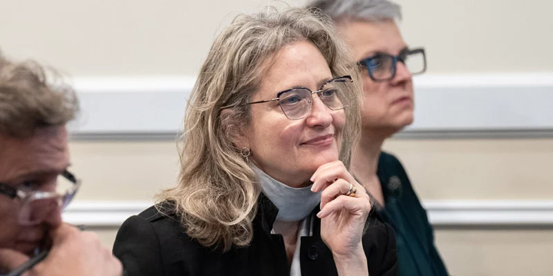 Close-up of conference attendees listening intently. A woman with blonde hair and glasses smiles slightly with her hand to her chin.