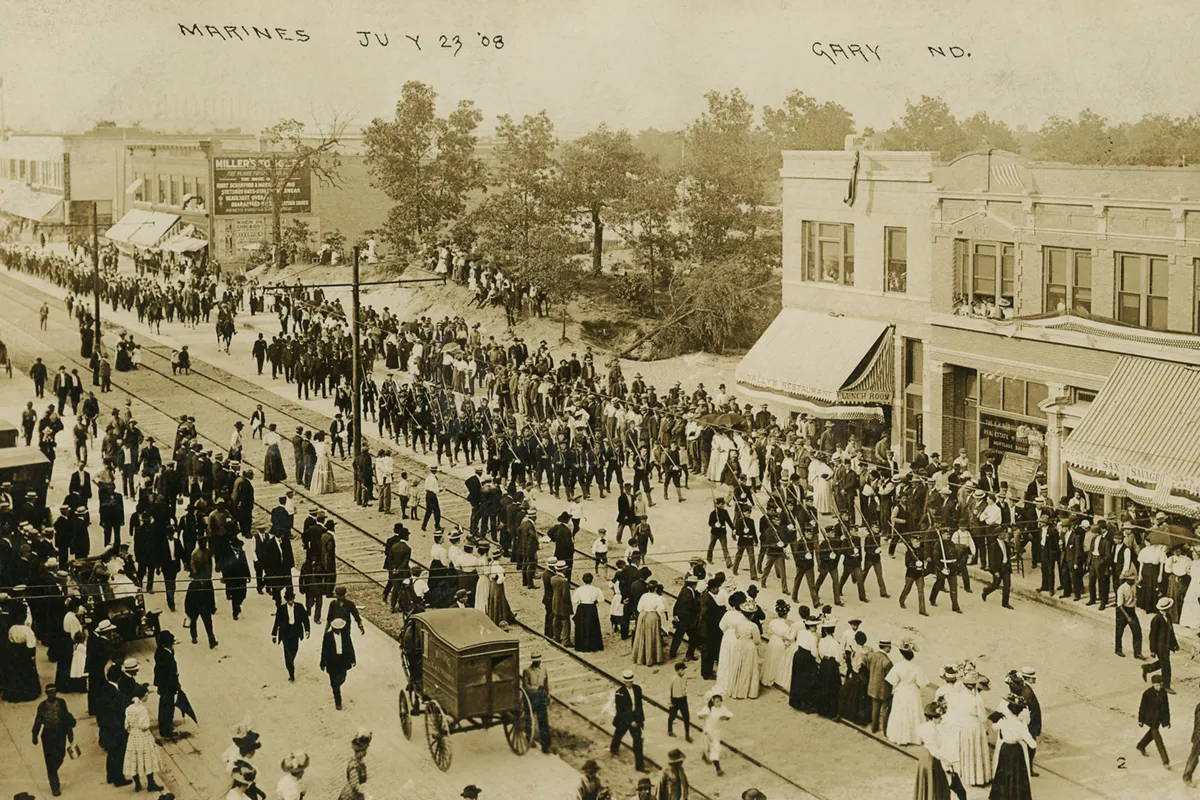 Sepia-toned archival photo showing Marines marching in a large parade down a crowded street in Gary, Indiana, on July 23, 1908.