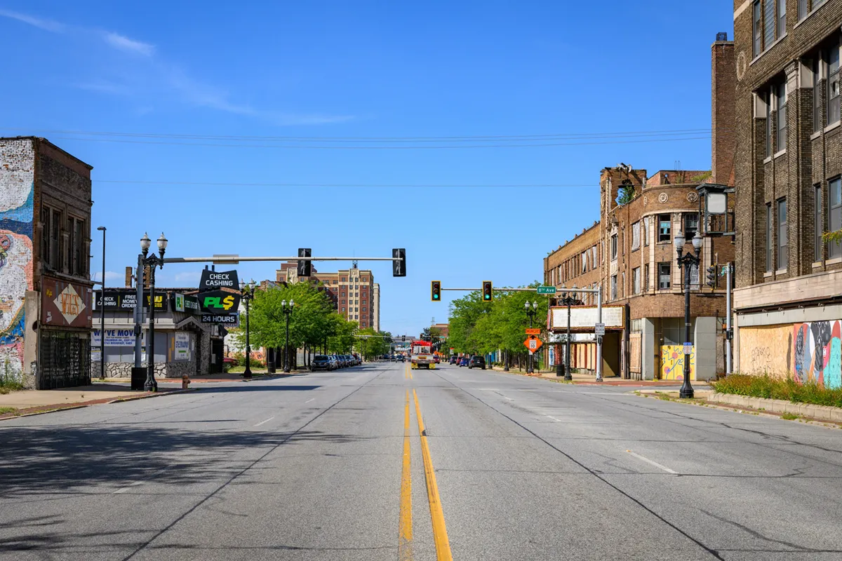 An urban street view of a wide, empty street with old brick buildings and traffic lights under a bright blue sky in Gary, Indiana.