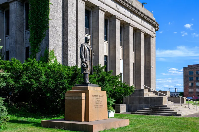 The statue of Elbert H. Gary stands on a pedestal in front of the columned facade of the old Gary City Hall building.