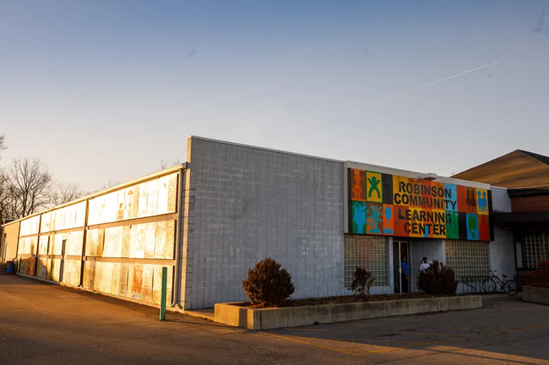 The former Robinson Community Learning Center building at golden hour, a modest white concrete block structure with a colorful painted sign and faded community murals along its exterior wall.