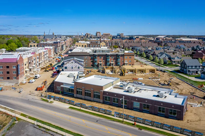 Aerial view of the Robinson Community Learning Center building under construction in South Bend, Indiana, with the Eddy Street Commons development and University of Notre Dame campus visible on the horizon under a clear blue sky.