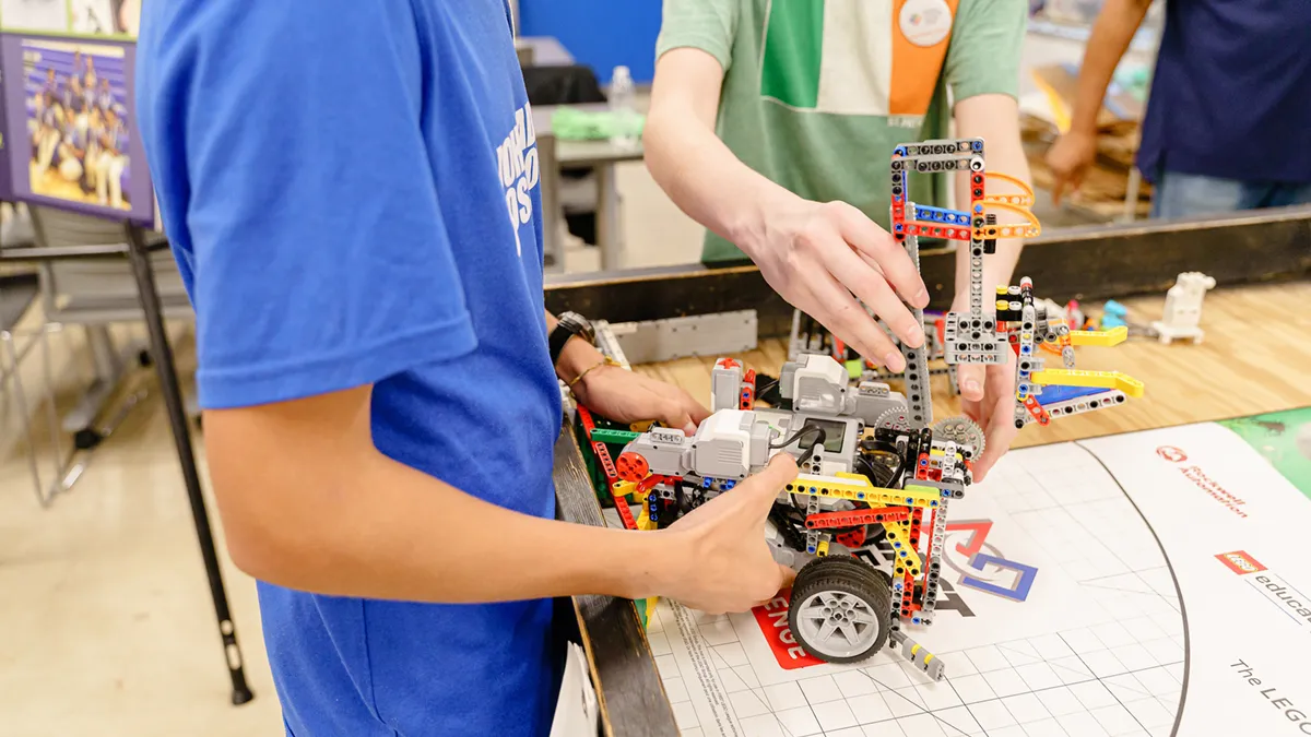 Two young people work together on a colorful LEGO Mindstorms robot on a competition mat.