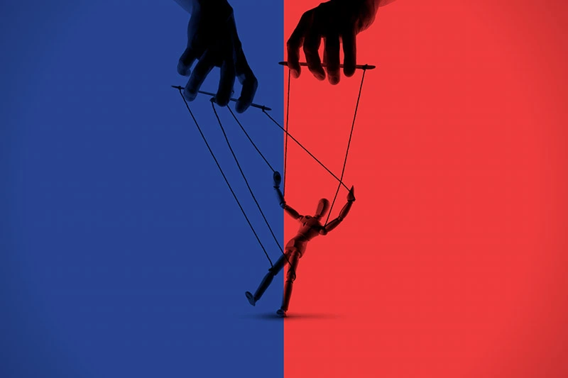 Silhouetted hands control a wooden puppet with strings. The background is sharply divided, blue on the left and red on the right, with the puppet centered on the color line, illuminated by both hues.