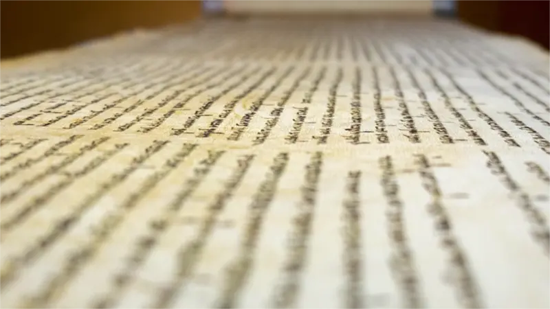 A close-up, shallow depth-of-field shot of an ancient parchment of the dead sea scrolls covered in dense lines of dark, handwritten text.