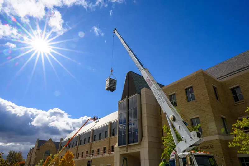 A construction machine lifts a stack of green roof plant tiles to the roof of the Mendoza College of Business building.
