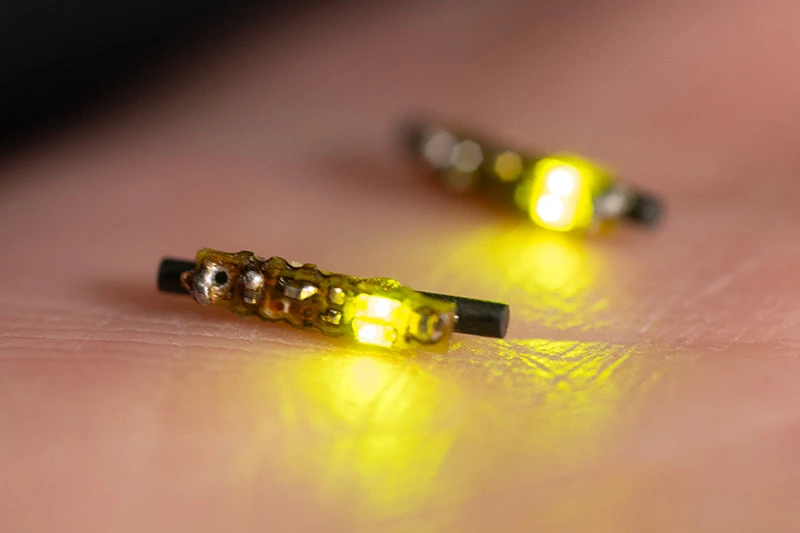 Two small, yellow-glowing electronic devices with visible circuitry on human skin.