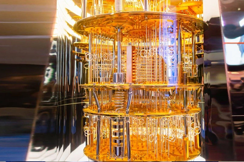 Intricate golden and silver quantum computer, featuring cylindrical stacked plates, numerous thin wires, and rods, illuminated by a subtle blue glow.