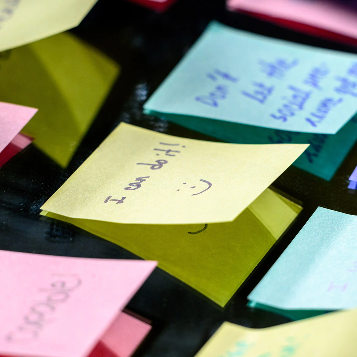 Close-up of several colorful sticky notes on a dark, reflective surface. A yellow note in focus reads &ldquo;I can do it!&rdquo; with a smiley face. Other pink, blue, and yellow notes are visible.