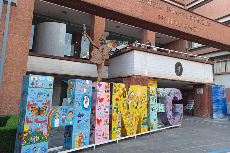 Large, colorful, painted letters spelling &ldquo;HIFG&rdquo; stand in front of the Hospital Infantil de México Federico Gómez building.