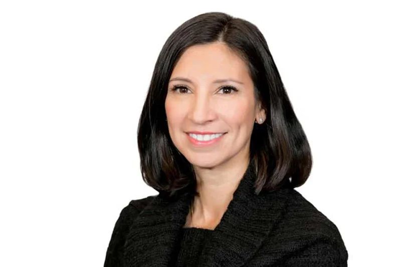 Professional headshot of a smiling woman with dark hair in a black textured top.