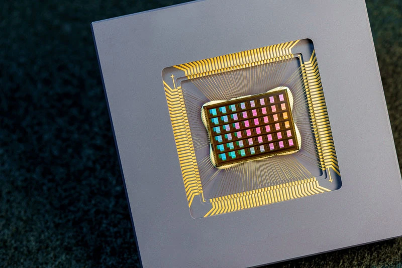 Close-up of a colorful, square semiconductor microchip wire-bonded within a gray casing.